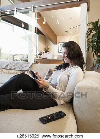 Stock Photography - Woman using tablet while sitting on couch. Fotosearch