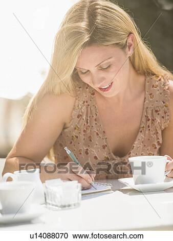 Stock Image - Woman writing journal at outdoor cafe table. Fotosearch