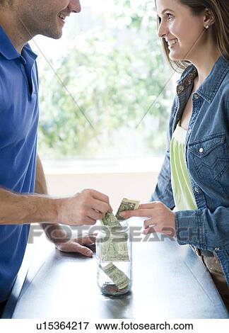 Young couple putting money in jar together View Large Photo Image Stock Photo - Young couple putting money in jar together. Fotosearch