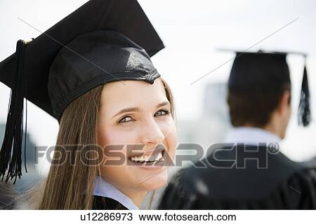 Stock Image - Young man and woman wearing graduation gowns. Fotosearch