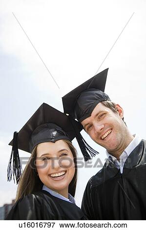 Stock Photo - Young man and woman wearing graduation gowns. Fotosearch