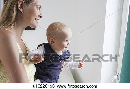 Stock Image - Young mother with daughter looking through window. Fotosearch