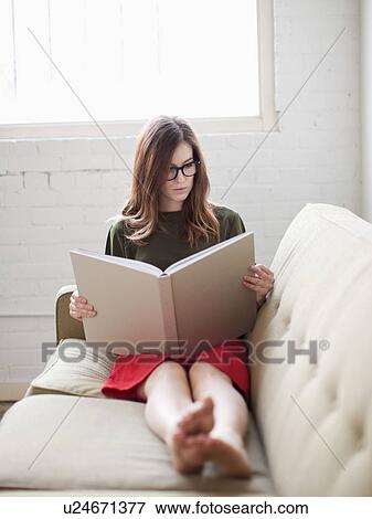 Stock Photo - Young woman on sofa reading book. Fotosearch