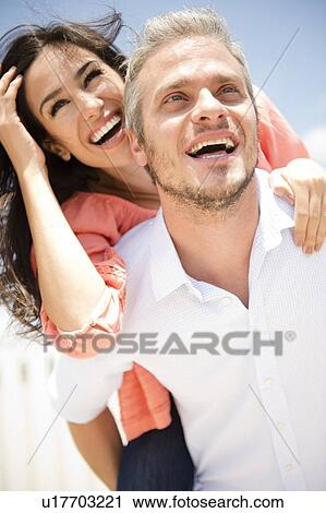 Stock Image - Young woman piggy back riding on man. Fotosearch