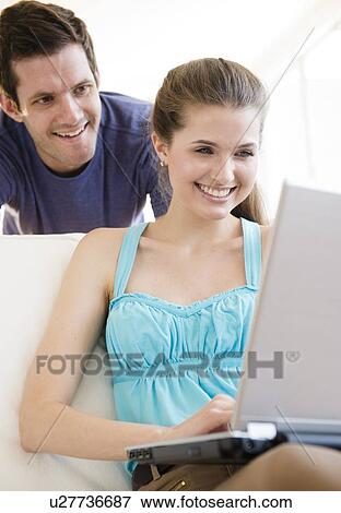 Stock Photo - Young woman using laptop while man is looking over her shoulder. Fotosearch