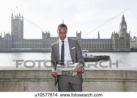 Picture - African American businessman reading newspaper with building in background. Fotosearch