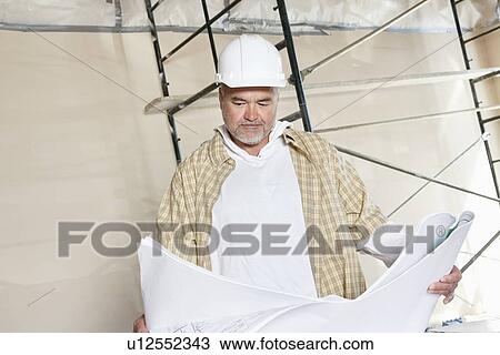 Stock Image - Architect looking at building plans with scaffold in background. Fotosearch