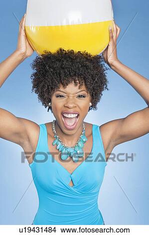 Picture - Attractive African American woman holding beach ball aloft over colored background. Fotosearch