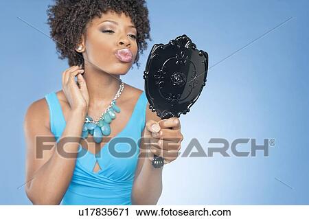 Stock Image - Attractive African American woman puckering while looking in mirror over colored background. Fotosearch