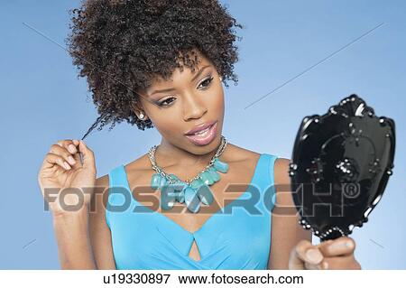 Attractive African American woman looking at herself in mirror over colored background View Large Photo Image Stock Photo - Attractive African American woman looking at herself in mirror over colored background. Fotosearch