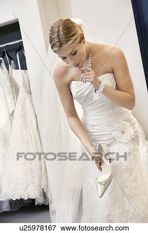 Beautiful confused woman in wedding dress holding footwear while looking down View Large Photo Image Stock Photo - Beautiful confused woman in wedding dress holding footwear while looking down. Fotosearch