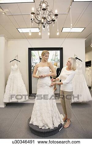 Stock Image - Beautiful woman dressed up as bride with senior employee helping in bridal store. Fotosearch