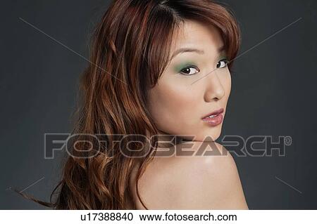 Stock Image - Beautiful young Chinese woman looking back over colored background. Fotosearch