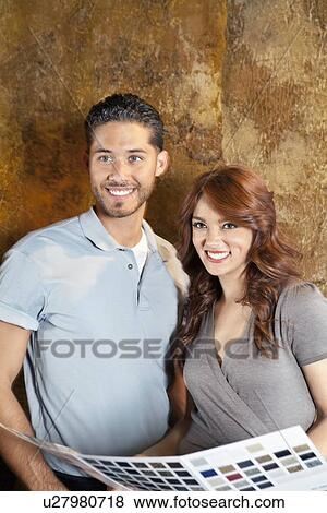 Stock Photo - Beautiful young couple with color samples smiling while looking away. Fotosearch