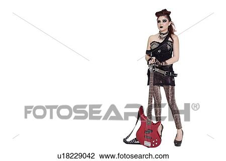 Stock Image - Beautiful young punk woman standing with guitar over white background. Fotosearch