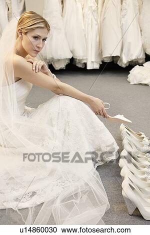 Stock Image - Beautiful young woman confused with footwear selection in bridal store. Fotosearch