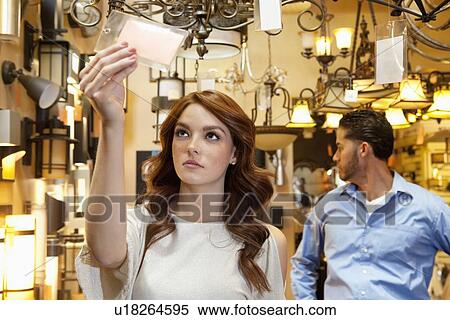 Beautiful young woman looking at price tag with man browsing in background View Large Photo Image Stock Photography - Beautiful young woman looking at price tag with man browsing in background. Fotosearch