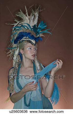 Beautiful young woman wearing costume with feather headgear over colored background View Large Photo Image Stock Photograph - Beautiful young woman wearing costume with feather headgear over colored background. Fotosearch