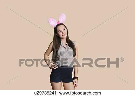 Beautiful young woman wearing rabbit ears while looking away over colored background View Large Photo Image Stock Image - Beautiful young woman wearing rabbit ears while looking away over colored background. Fotosearch
