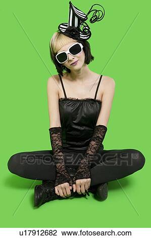Beautiful young woman wearing sunglasses and headgear while sitting with legs crossed over green background View Large Photo Image Stock Image - Beautiful young woman wearing sunglasses and headgear while sitting with legs crossed over green background. Fotosearch
