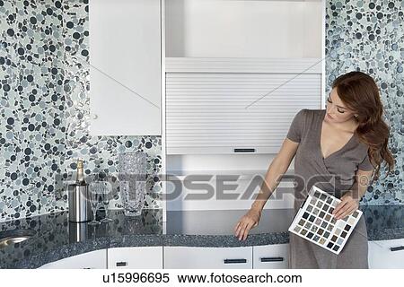 Stock Photography - Beautiful young woman with color samples looking at contemporary kitchen cabinets. Fotosearch