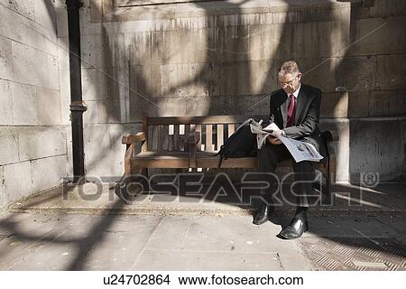 Businessman sitting on outdoor bench reading newspaper View Large Photo Image Picture - Businessman sitting on outdoor bench reading newspaper. Fotosearch
