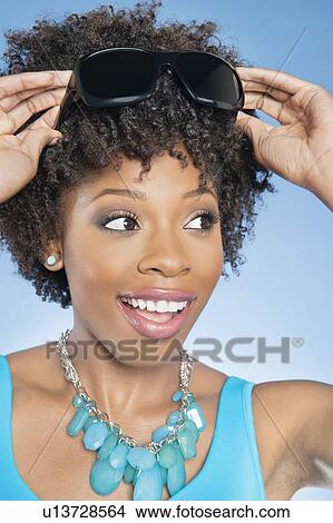 Cheerful African American woman adjusting sunglasses over colored background View Large Photo Image Picture - Cheerful African American woman adjusting sunglasses over colored background. Fotosearch