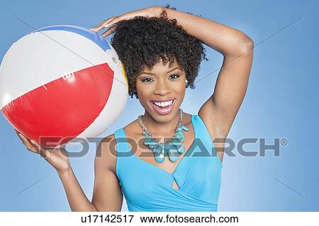 Stock Photo - Cheerful African American woman with beach ball over colored background. Fotosearch