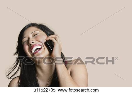 Stock Photography - Cheerful young woman talking on mobile phone over colored background. Fotosearch
