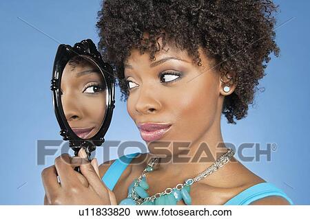 Close-up of African American woman looking at herself in mirror over colored background View Large Photo Image Stock Image - Close-up of African American woman looking at herself in mirror over colored background. Fotosearch