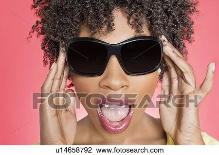 Stock Image - Close-up of an African American woman wearing sunglasses over colored background. Fotosearch
