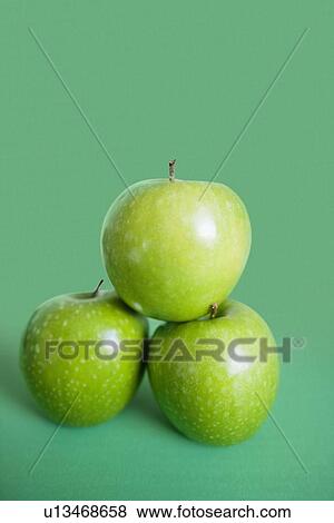 Stock Photo - Close-up of green apples in pyramid stack over colored background. Fotosearch