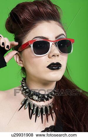 Close-up of young punk woman wearing sunglasses over green background View Large Photo Image Stock Photo - Close-up of young punk woman wearing sunglasses over green background. Fotosearch