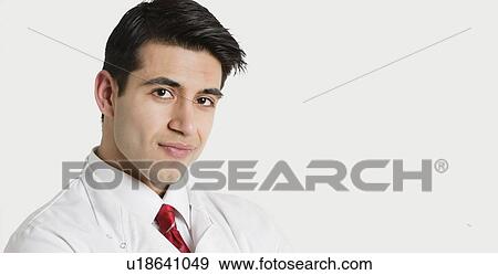 Stock Photo - Close-up portrait of a handsome Indian male doctor smiling over light gray background. Fotosearch