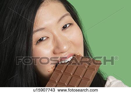 Close-up portrait of a young woman eating chocolate over green background View Large Photo Image Stock Image - Close-up portrait of a young woman eating chocolate over green background. Fotosearch