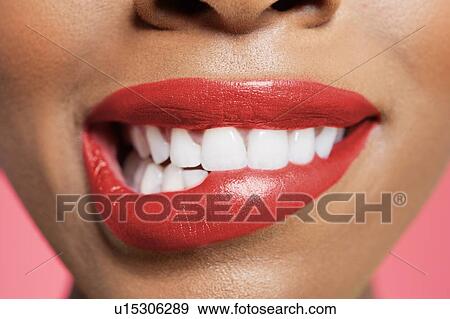Stock Photo - Close-up view of an female biting her red lip over colored background. Fotosearch