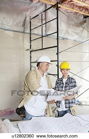 Construction team looking at paper with blueprints on table View Large Photo Image Stock Image - Construction team looking at paper with blueprints on table. Fotosearch
