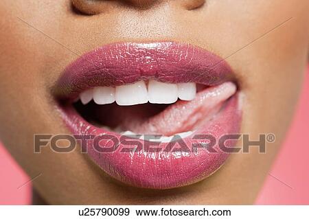 Stock Photo - Cropped image of woman licking pink lipstick. Fotosearch
