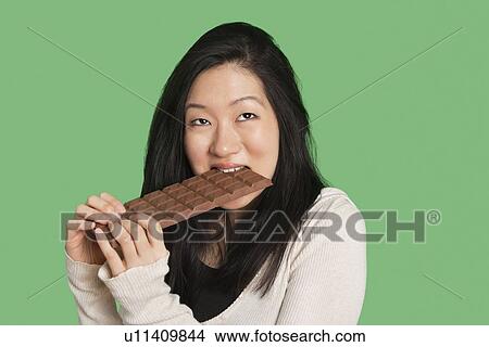 Cute young woman eating a large chocolate bar over green background View Large Photo Image Picture - Cute young woman eating a large chocolate bar over green background. Fotosearch