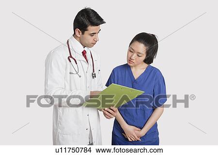Doctor discussing medical report with female nurse over gray background View Large Photo Image Picture - Doctor discussing medical report with female nurse over gray background. Fotosearch