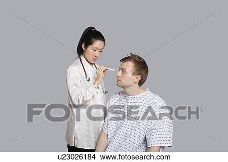 Picture - Doctor examining patient's eye with flashlight. Fotosearch