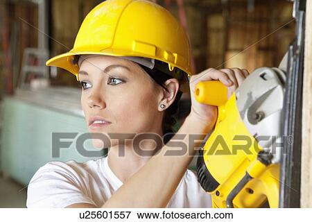 Stock Photo - Female construction worker cutting wood with a power saw while looking away. Fotosearch
