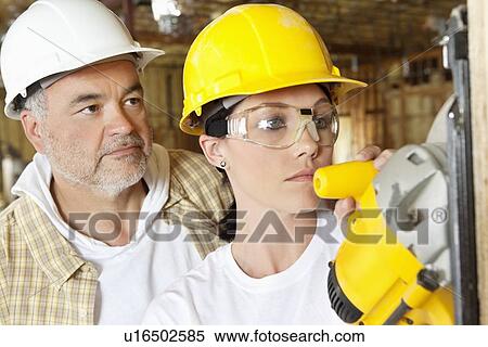Female worker cutting wood with a power saw while male worker standing behind View Large Photo Image Stock Photography - Female worker cutting wood with a power saw while male worker standing behind. Fotosearch