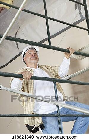 Stock Image - Front view of mature man climbing scaffold. Fotosearch