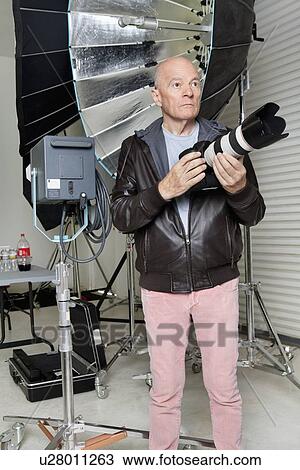 Stock Image - Front view of senior man with camera in photographer's studio. Fotosearch