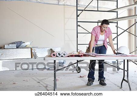 Front view of young female contractor looking at building plans at table View Large Photo Image Picture - Front view of young female contractor looking at building plans at table. Fotosearch