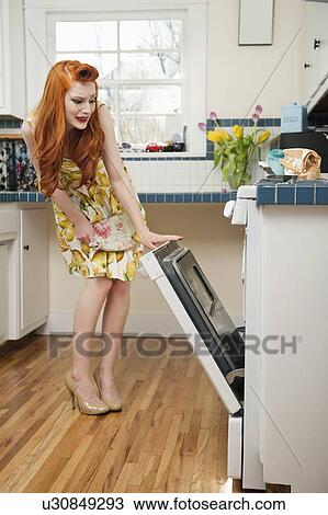 Full length of a young redheaded woman looking into an open oven View Large Photo Image Stock Image - Full length of a young redheaded woman looking into an open oven. Fotosearch