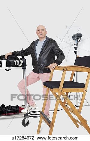 Stock Image - Full length portrait of a happy senior photographer with equipments in studio. Fotosearch