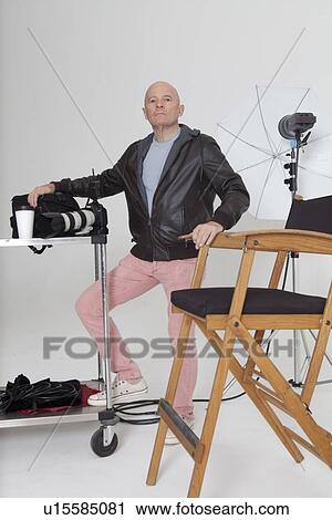 Stock Image - Full length portrait of senior photographer with equipments in studio. Fotosearch