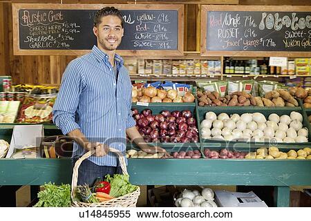 Handsome young man holding basket at vegetable stall in supermarket View Large Photo Image Stock Photography - Handsome young man holding basket at vegetable stall in supermarket. Fotosearch